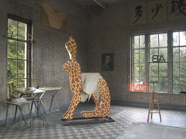 interieur van het atelier met o.a. de Giraf, een werk in uitvoering. Het beeld wordt in cortenstaal gemaakt. Links boven op de muur een papieren vlindervorm. Deze vorm is een werk in uitvoering en wordt in 80 mm dik zwart graniet uitgehakt en gepolijst