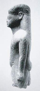 Kouros, linkerzijde, een kleine stenen naakte jongen. Het is een votiefgeschenk uit de oriëntaliserende periode +/- 600 voor Chr., van de Grieken. Omdat het beeldje in Amsterdam te bezichtigen is heeft het de naam ‘de Amsterdamse Kouros’ gekregen.