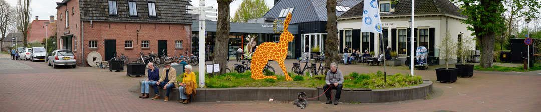 Kunstmoment Diepenheim 2023. Bezoekers pauzeren rond het beeld Dit is een giraf. Het beeld heeft de vorm van een haas met rechtopstaande oren en heeft de schutskleuren van een giraf.